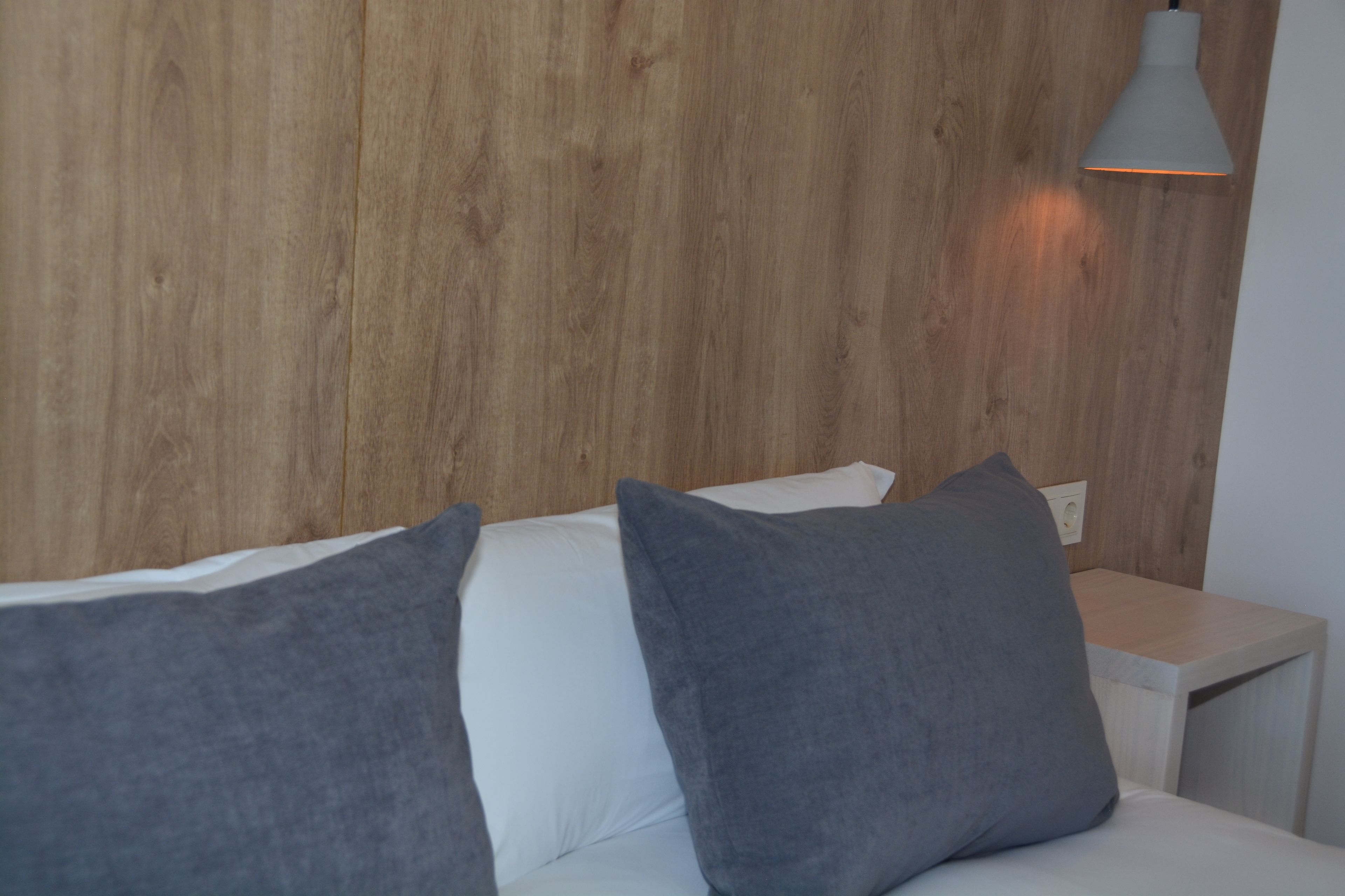 Een moderne slaapkamer met een houten hoofdbord, een witte nachtkastje en een grijs kussen.