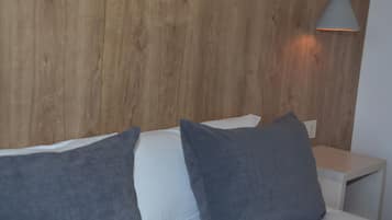 Een moderne slaapkamer met een houten hoofdbord, een witte nachtkastje en een grijs kussen.