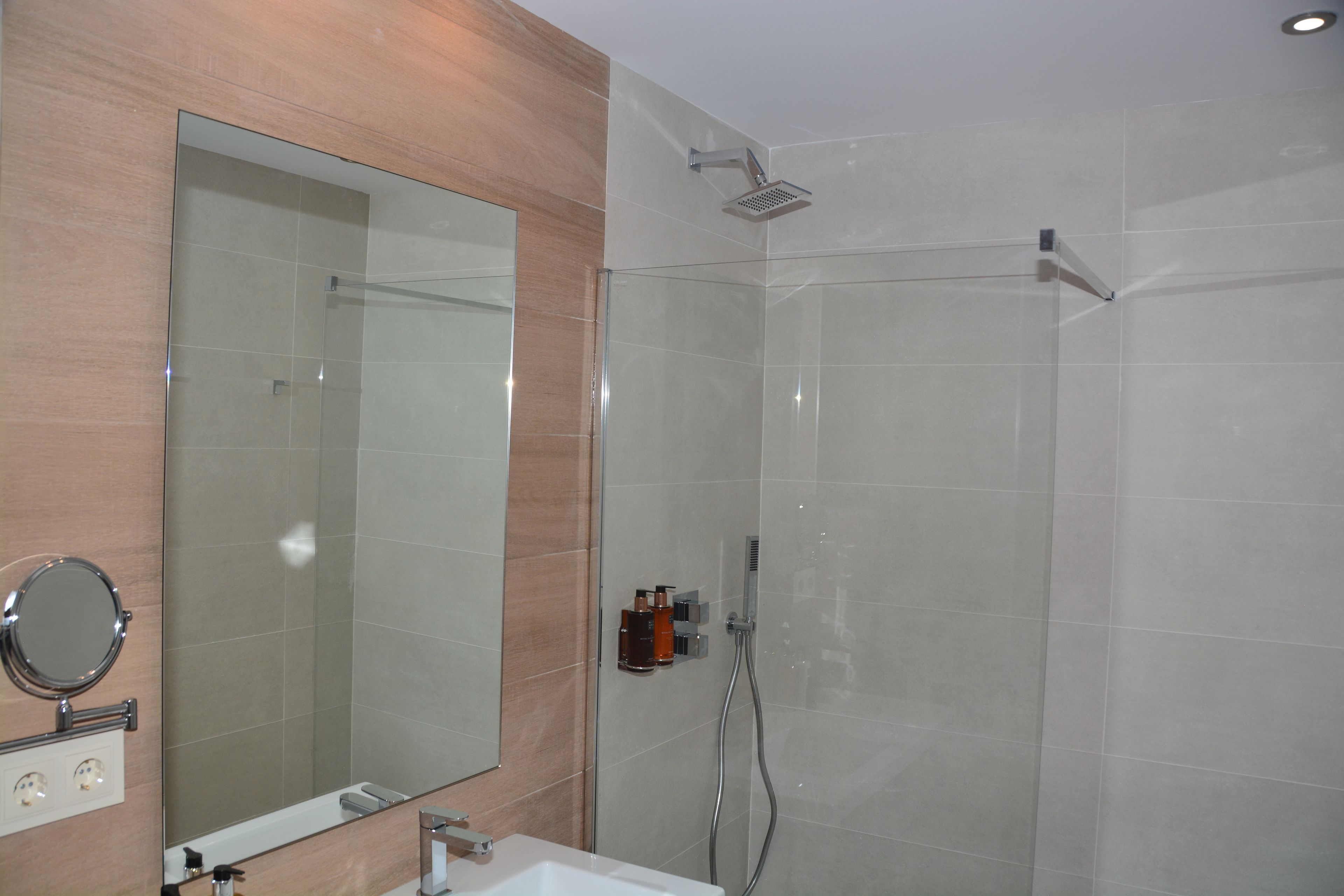 A modern bathroom with a glass shower enclosure, a large mirror, and a sink with a faucet.