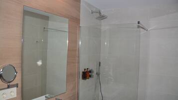 A modern bathroom with a glass shower enclosure, a large mirror, and a sink with a faucet.