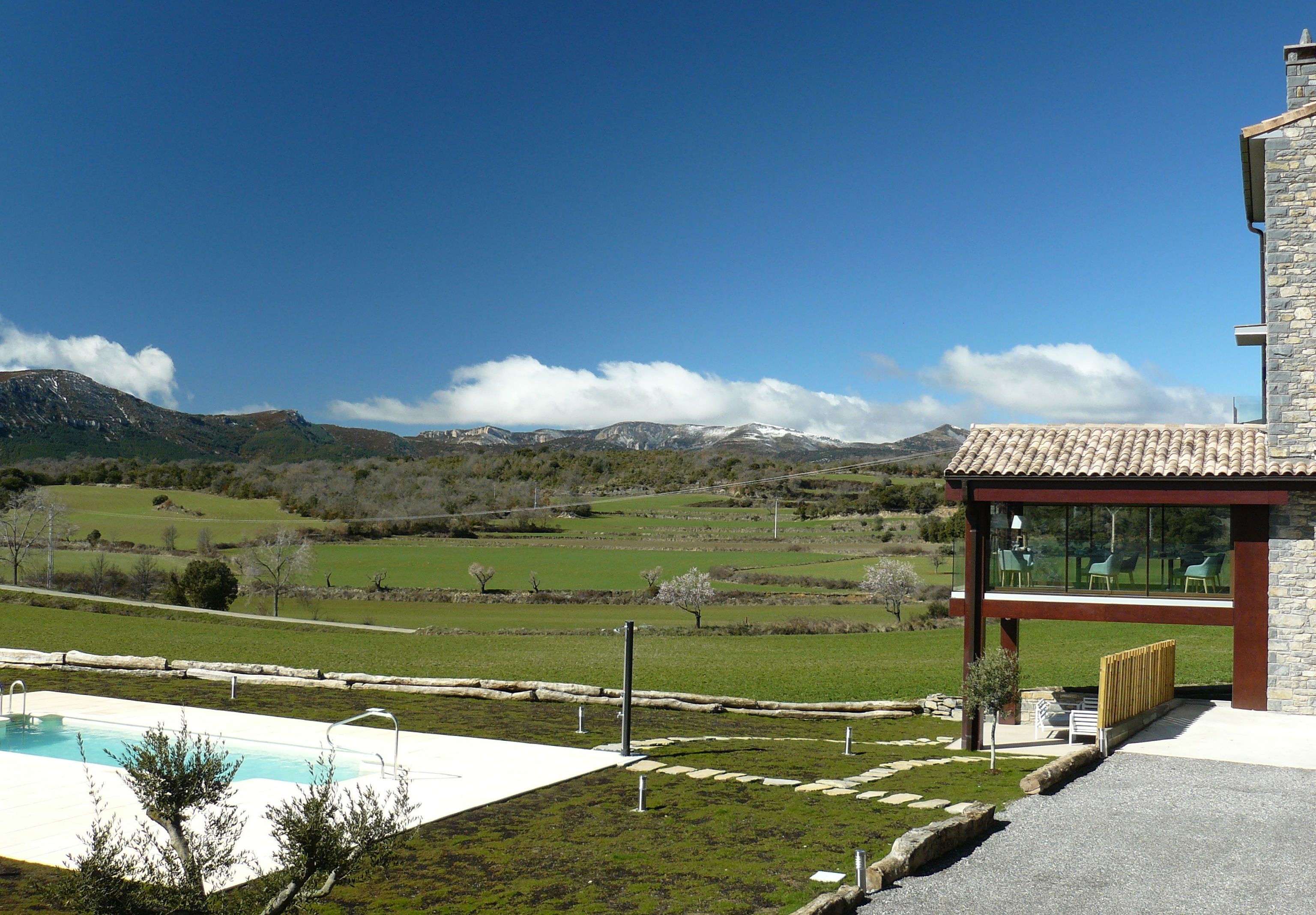 A modern house with a swimming pool, stone exterior, and a view of mountains.