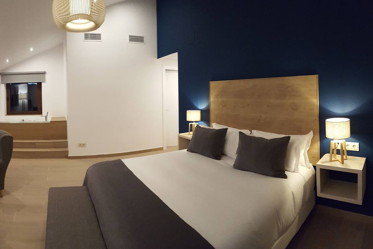 Een moderne hotelkamer met een groot bed, bedlampen, een bureau met stoel en een aan de muur bevestigde televisie.