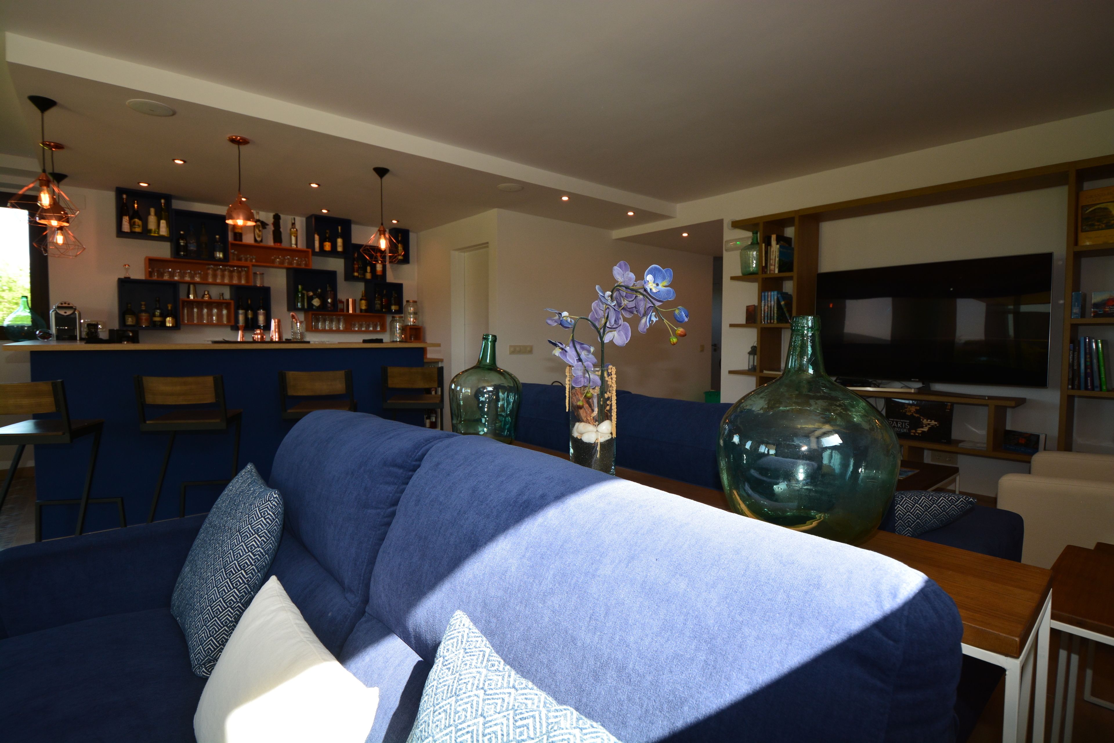 A modern living room with a blue sofa, decorative vases, and a bar area in the background.