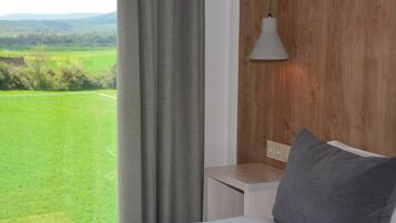 A bedroom with a view of a green field and mountains.
