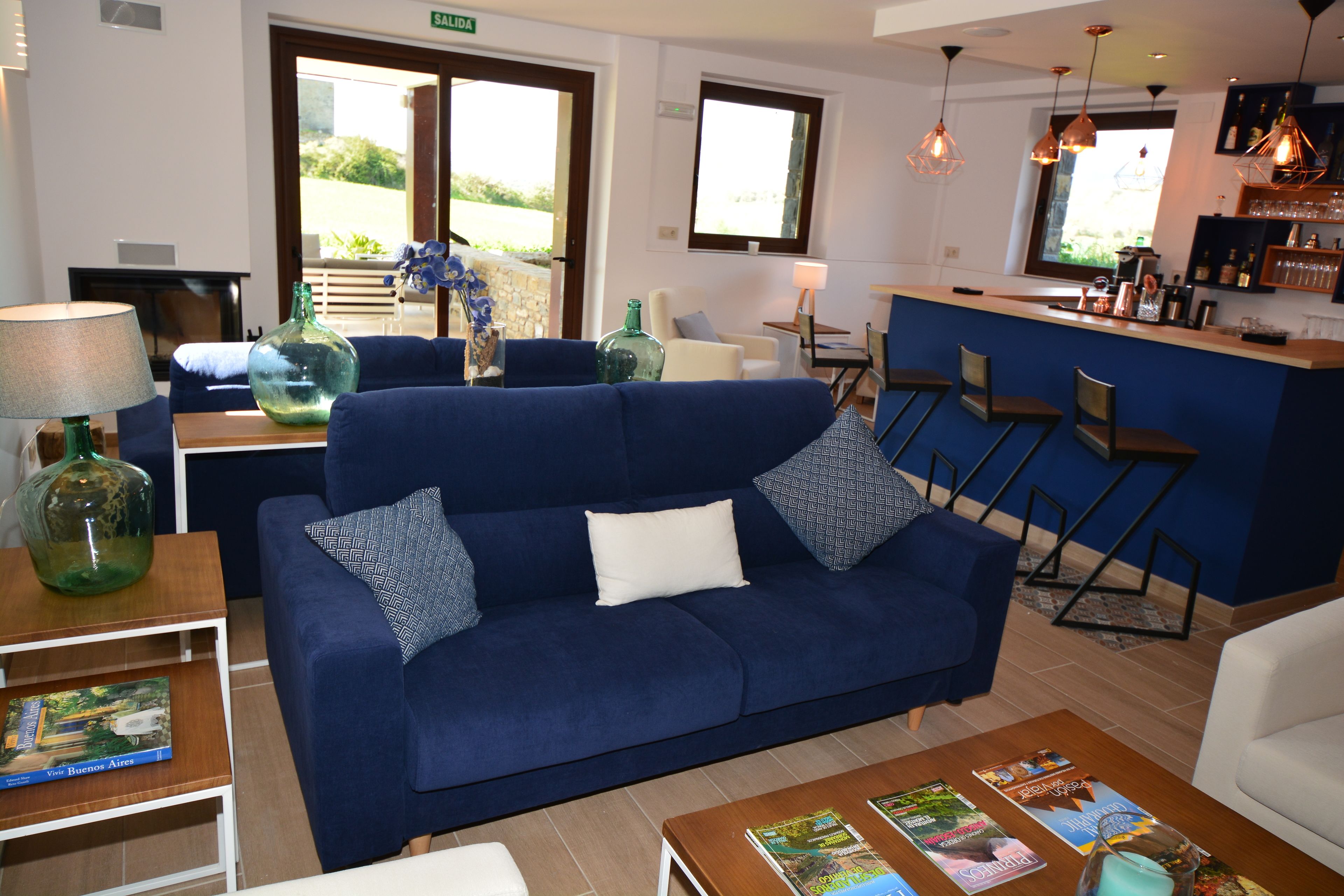 Un moderno vestíbulo de hotel con un sofá azul, una zona de bar y vistas al exterior.