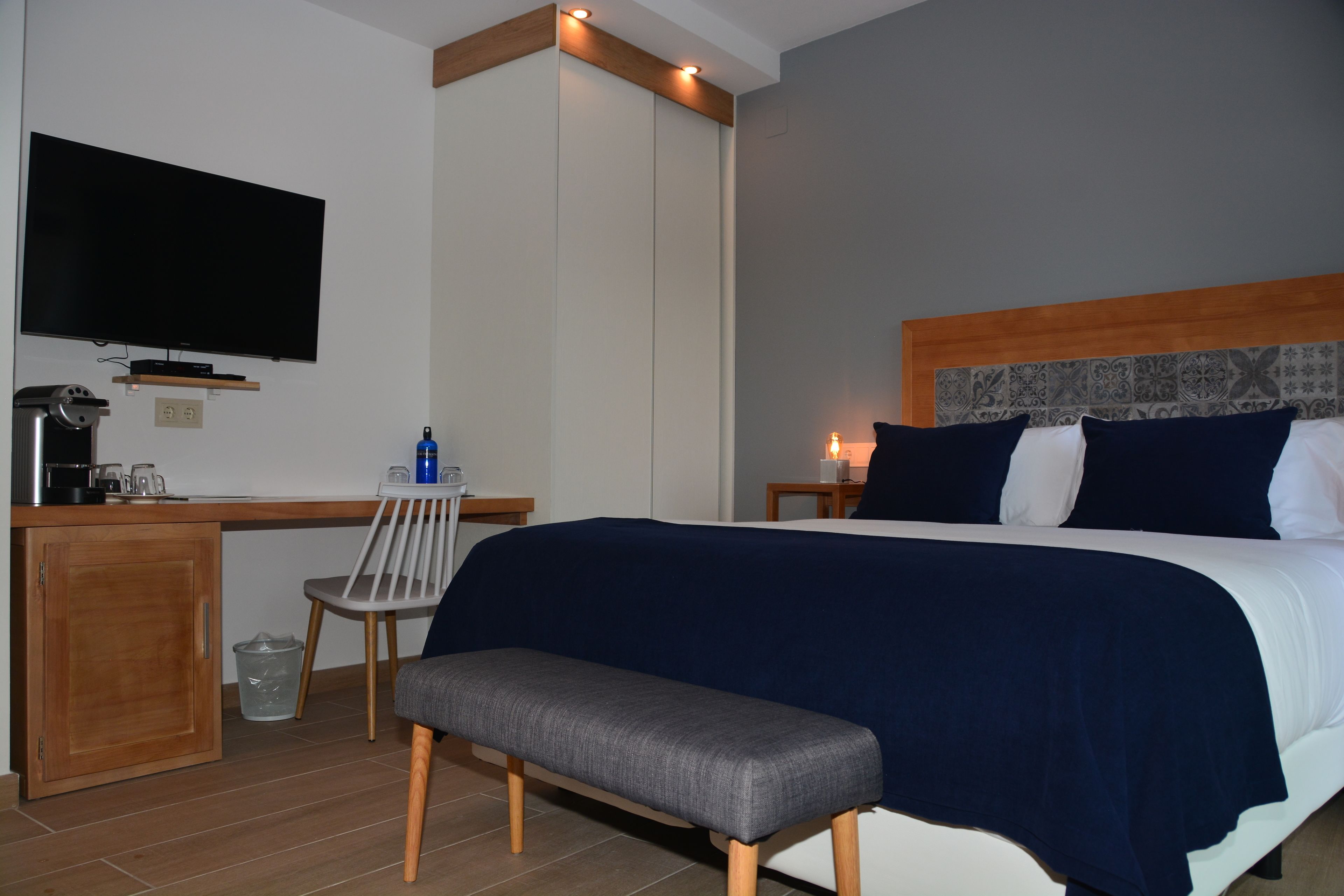 Una habitación de hotel con una cama, un escritorio con televisor, una silla y un banco.