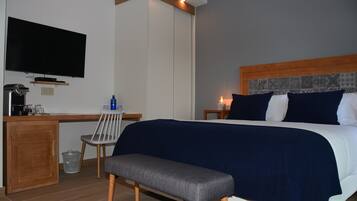 Una habitación de hotel con una cama, un escritorio con televisor, una silla y un banco.