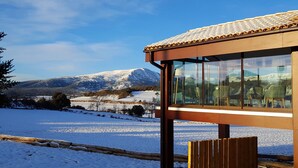 Ein modernes Gebäude mit großen Fenstern und Blick auf eine verschneite Landschaft und Berge.