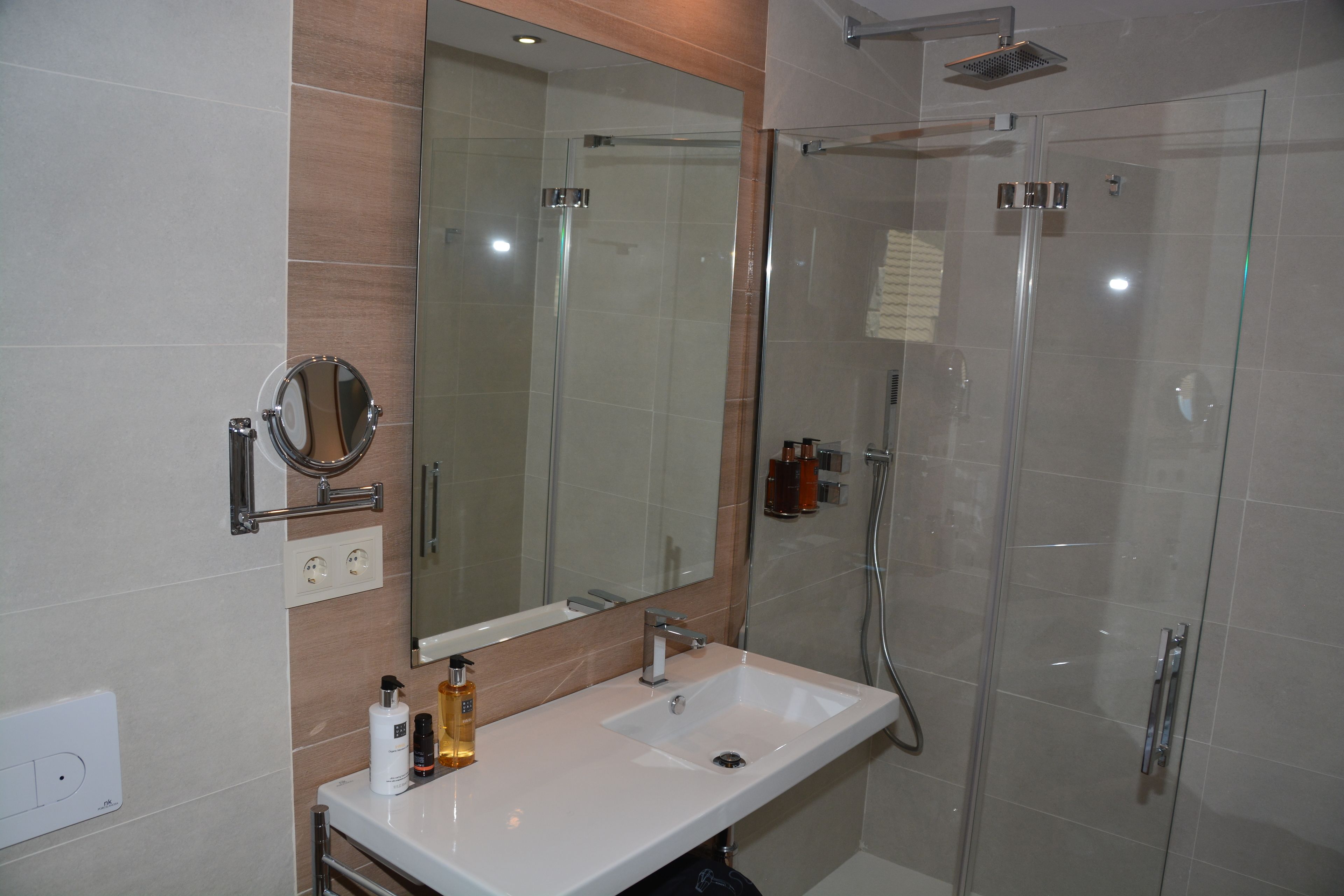 A modern bathroom with a glass-enclosed shower, a large mirror, and a white sink.