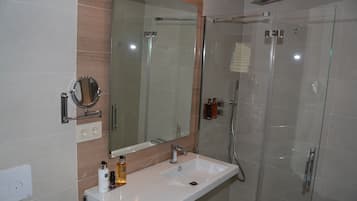 A modern bathroom with a glass-enclosed shower, a large mirror, and a white sink.