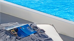 A magazine, sunglasses, and a towel on a boat's edge with a pool in the background.