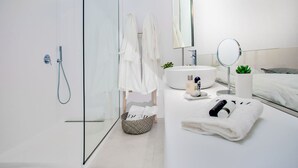 A modern bathroom with a glass shower enclosure, a white sink, a mirror, and a small potted plant.