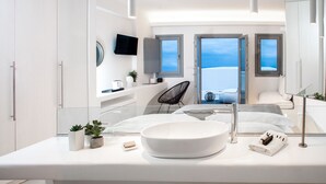 A modern bathroom with a large white sink, a mirror, and a view of the sea through open doors.