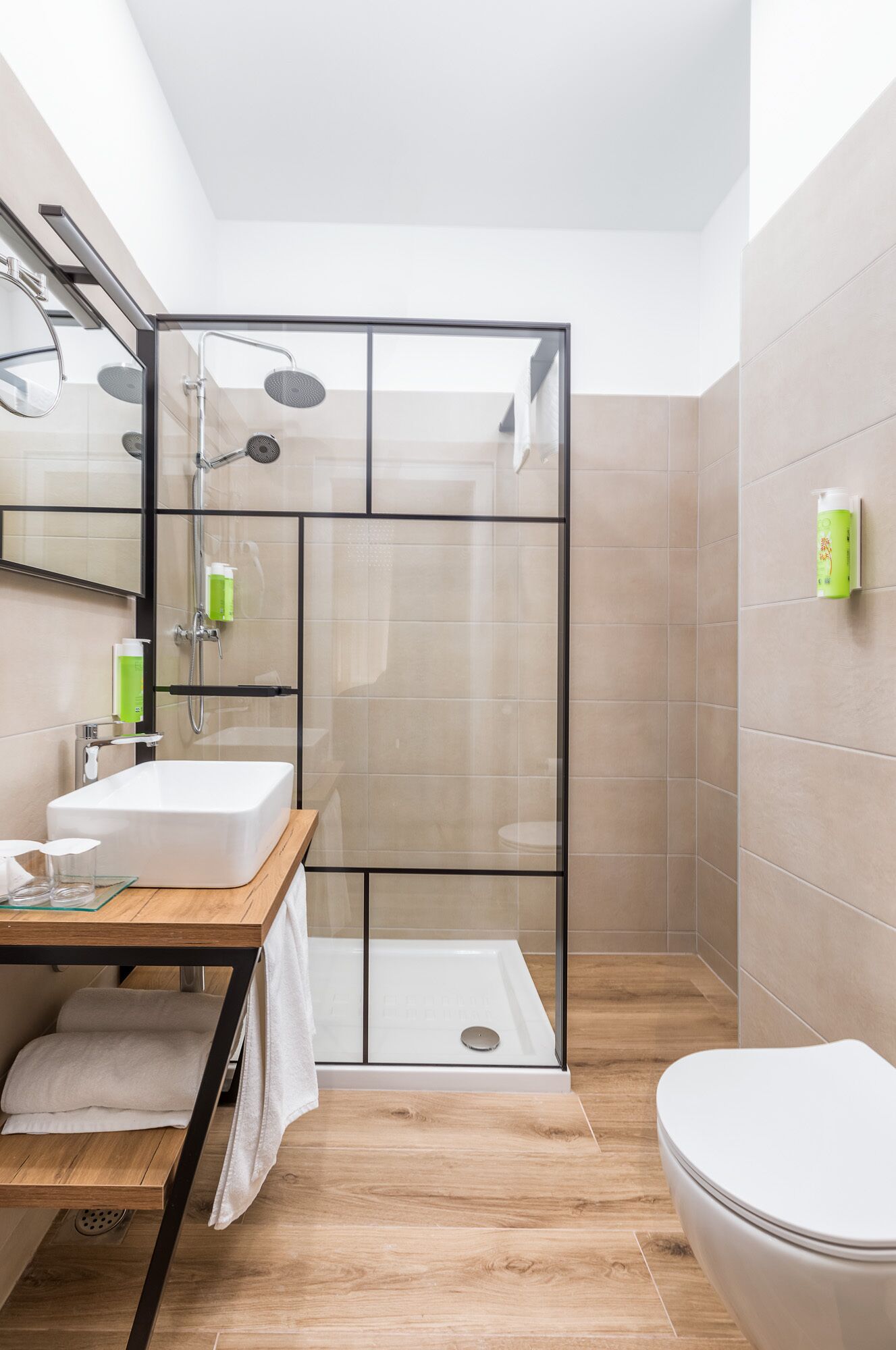 Un baño moderno con ducha envuelta en vidrio, tocador de madera, lavamanos blanco y un inodoro.