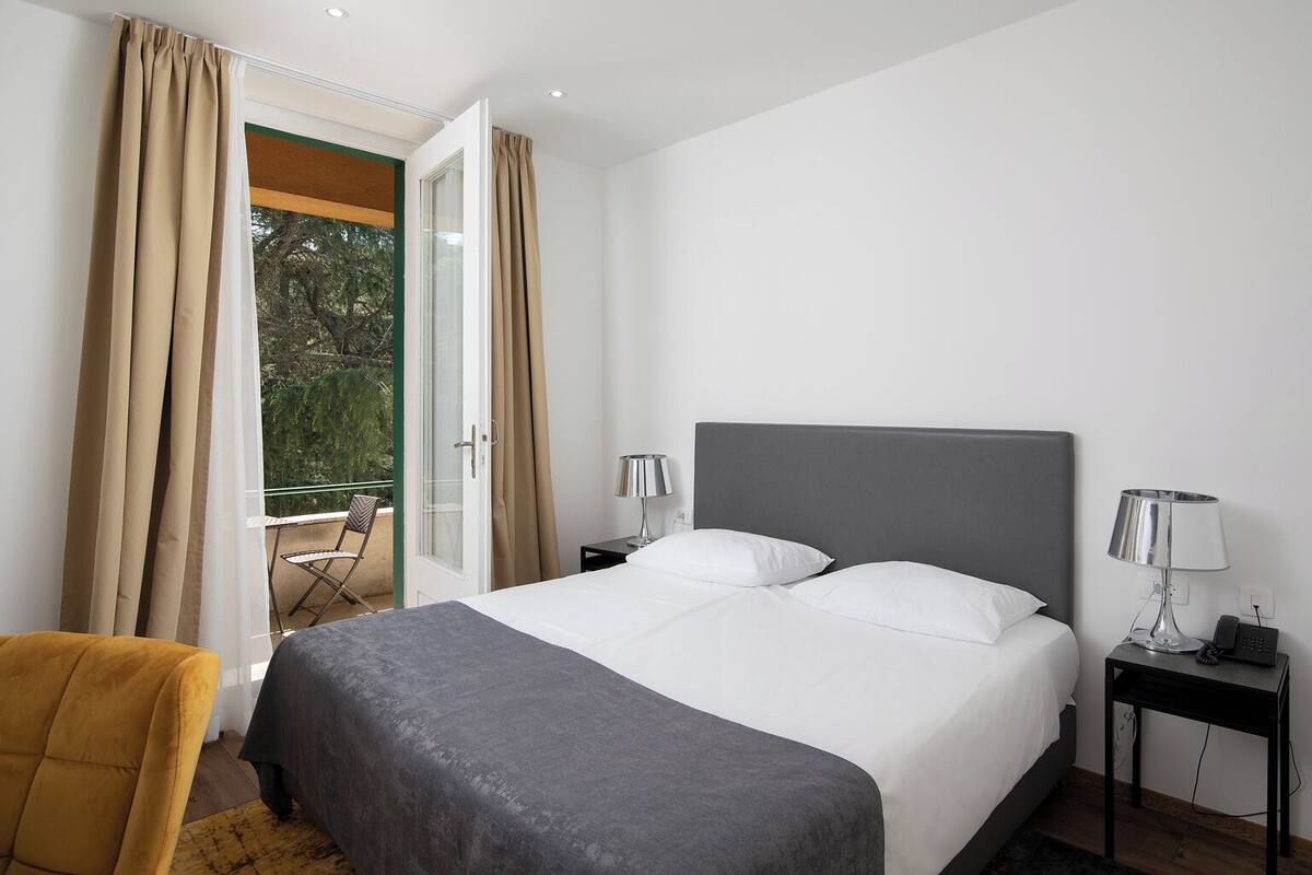 A hotel room with a bed, two bedside tables, a chair, and a balcony with curtains.