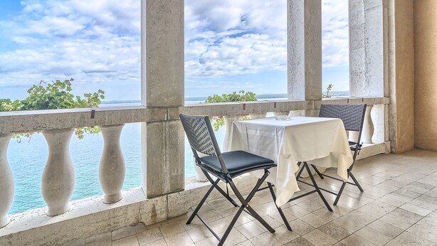 A balcony with a table and chairs, overlooking a body of water and greenery. - Brijuni Hotel Neptun (Pula)