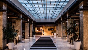 A spacious lobby with a central reception desk, large potted plants, and a glass ceiling. - Brijuni Hotel Neptun (Pula)
