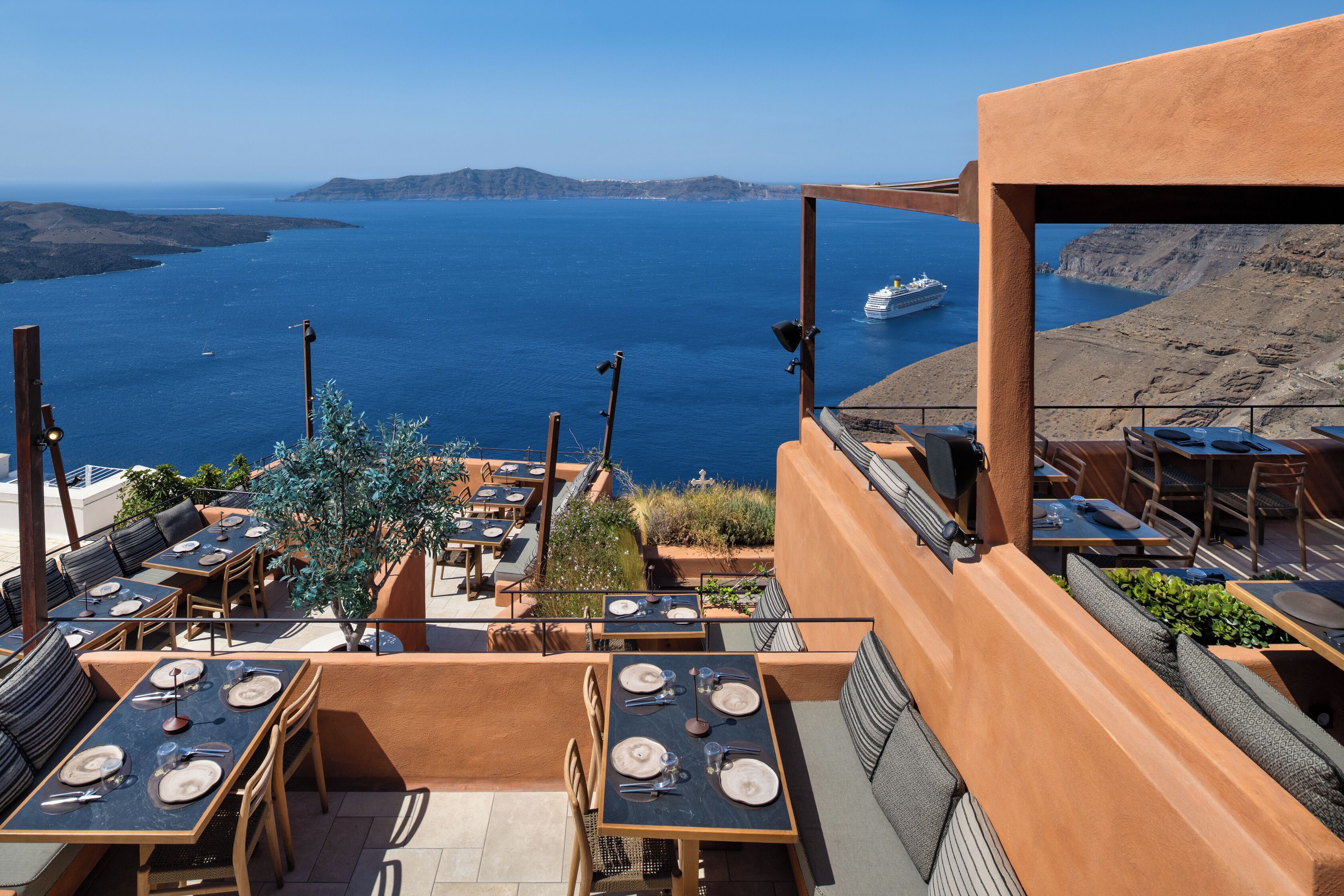 An outdoor dining area with tables set for two, overlooking a body of water and distant land.