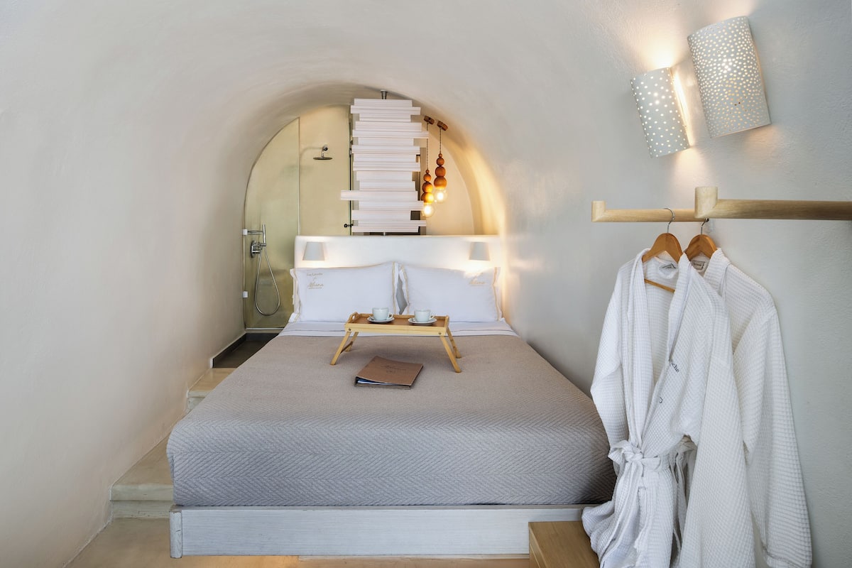 Quarto com cama, mesa de cabeceira, cabideiro suspenso e luminária fixada na parede.