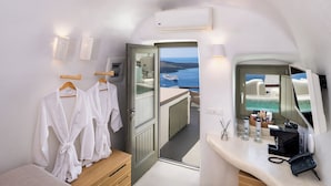 A hotel room with a balcony, a bed, a bathroom with a mirror, and a view of the sea. - Athina Aperto Suites (Santorini)