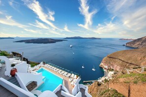 A resort with a pool, lounge chairs, and a view of the sea and islands. - Athina Aperto Suites (Santorini)