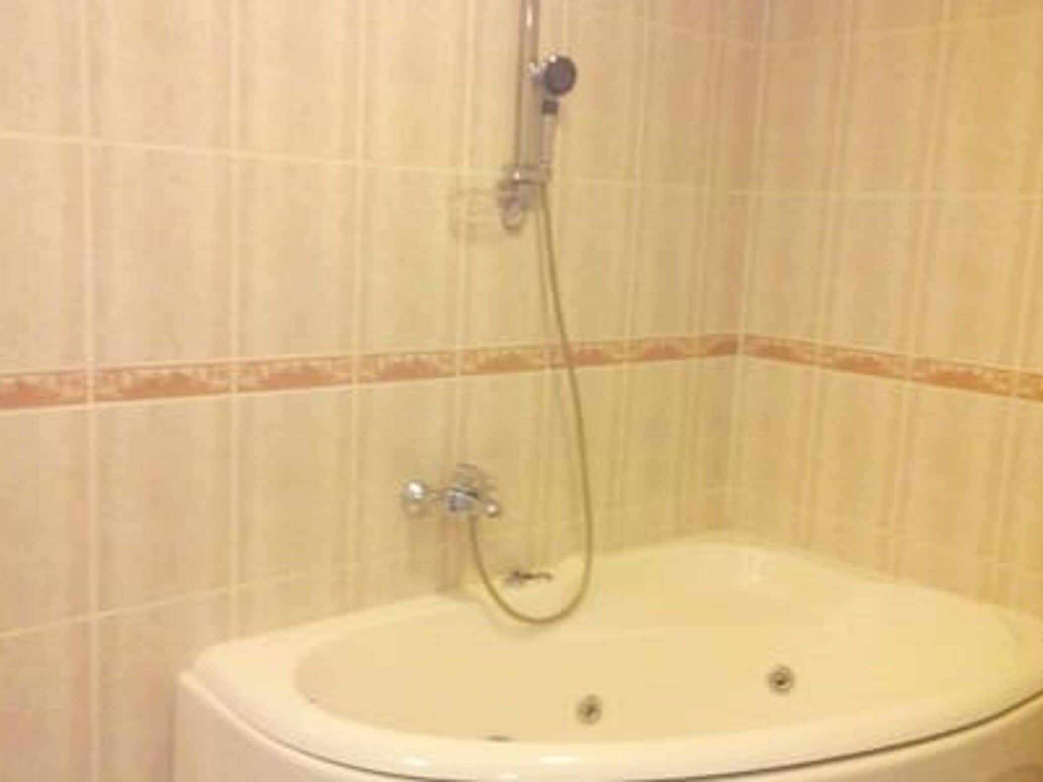 Un baño con una bañera blanca, un cabezal de ducha y una pared cubierta de azulejos.