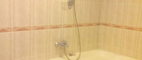 Un baño con una bañera blanca, un cabezal de ducha y una pared cubierta de azulejos.
