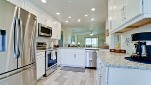 A modern kitchen with stainless steel appliances, white cabinetry, and a marble countertop. - Coastal Condo, Heated Pool Steps from the Beach (Holmes Beach)