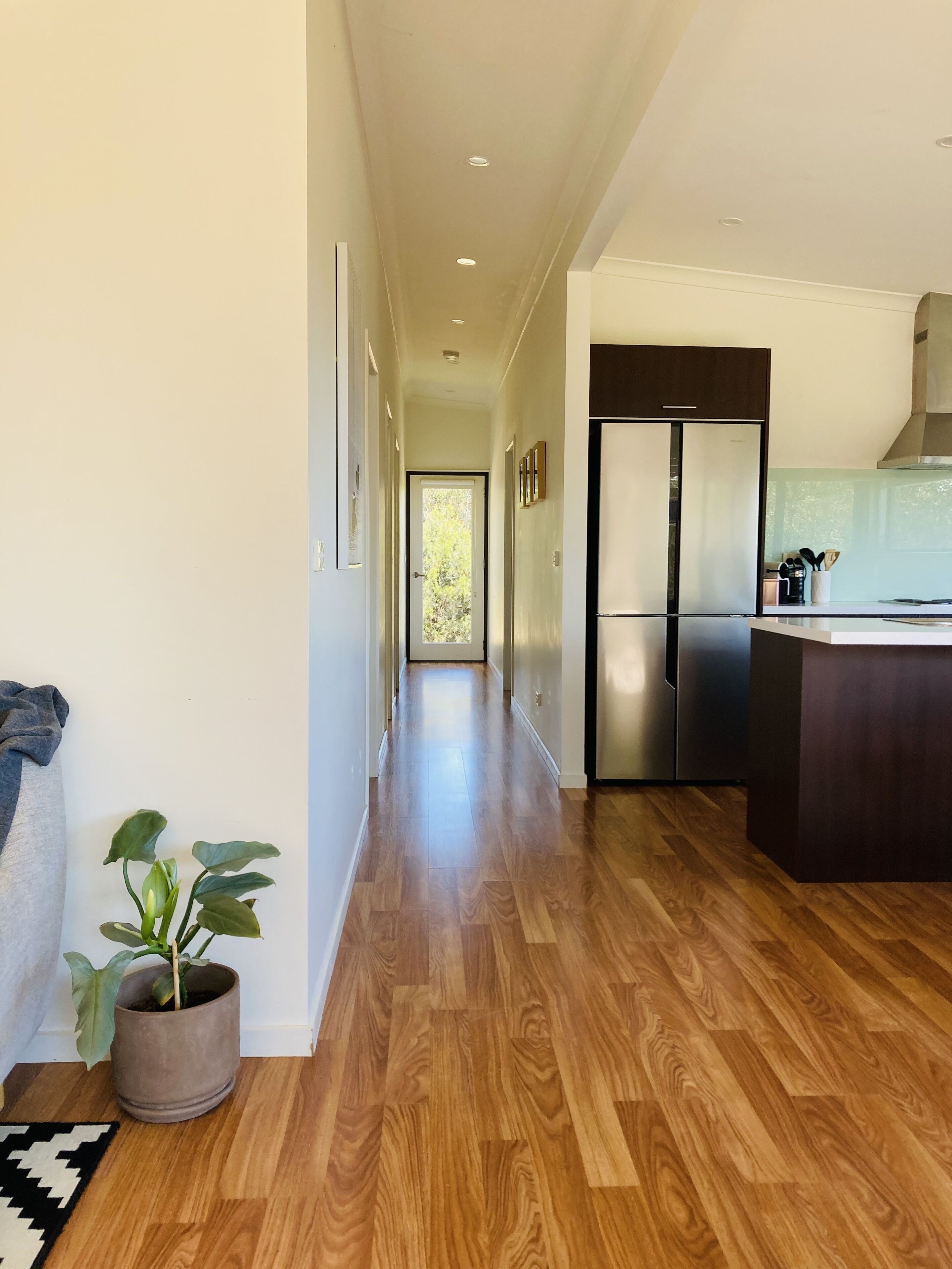 A modern kitchen with a stainless steel refrigerator, wooden flooring, and a view into the dining area.