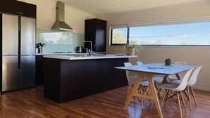 A modern kitchen with a central island, dark cabinetry, and a large window providing a view of the outdoors. - Architectural Design Rural Retreat (Forcett)