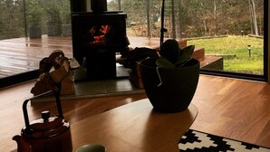 A cozy living room with a fireplace, a wooden table, and a view of the outdoors. - Architectural Design Rural Retreat (Forcett)