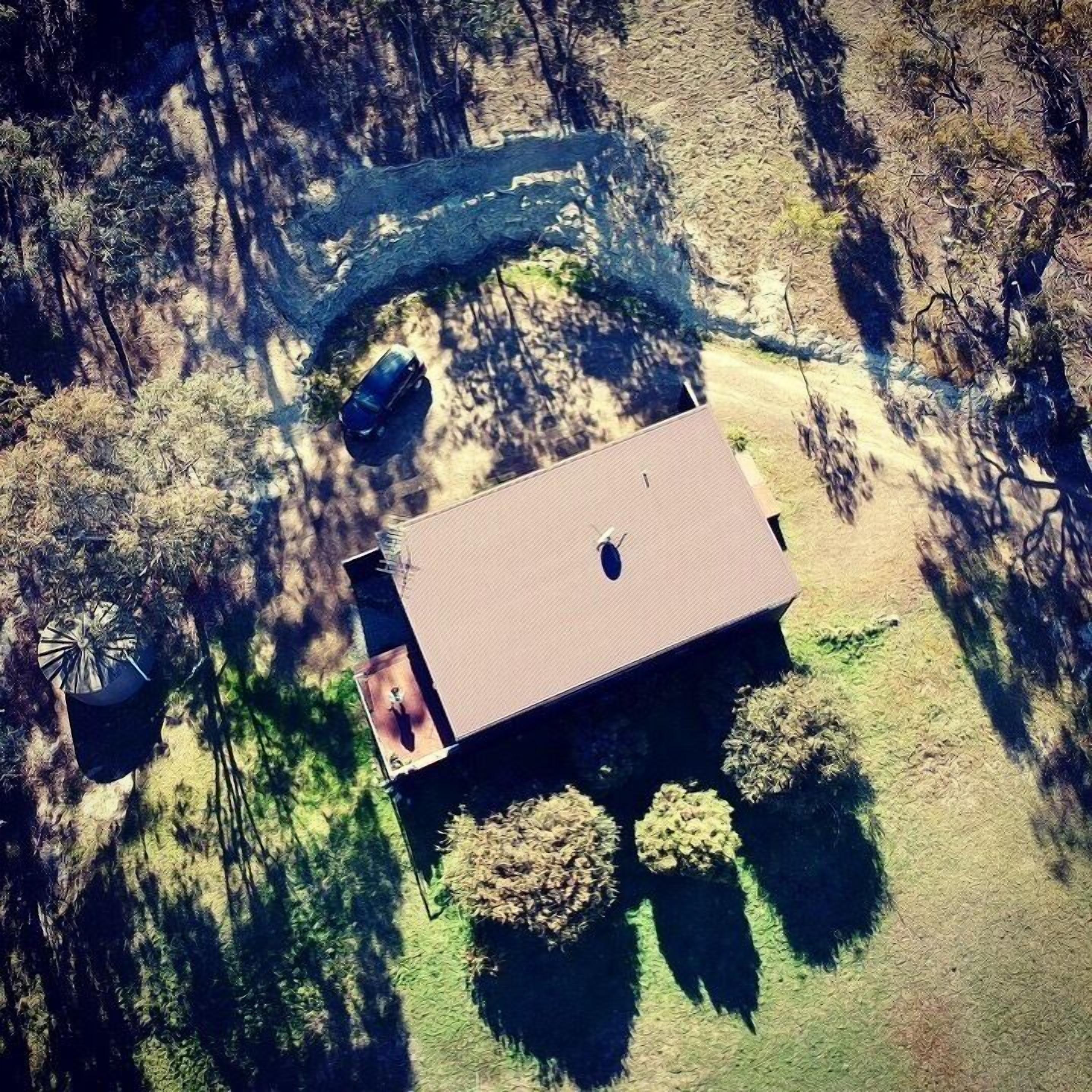 Une vue aérienne d’une maison avec un toit plat, une terrasse bien visible et un véhicule garé à proximité.
