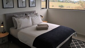 A bedroom with a large bed, a window with a view of the countryside, and three framed pictures on the wall. - Architectural Design Rural Retreat (Forcett)