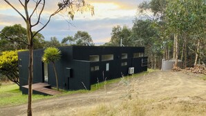 A modern black building with multiple windows and a satellite dish, surrounded by dry grass and trees. - Architectural Design Rural Retreat (Forcett)