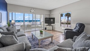 A spacious living room with a large glass door leading to a balcony, a flat-screen TV, and a comfortable seating area with sofas and chairs. - Island House Beach Resort 3S (Siesta Key)