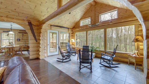 Ein Holzhütten-Interieur mit Holzbalkendecke, großen Fenstern, einem Essbereich und einer Sitzecke mit Stühlen und einer Couch.