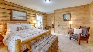 Ein Schlafzimmer einer Holzhütte mit Bett, Bank, Stuhl und zwei Bildern an den Wänden.