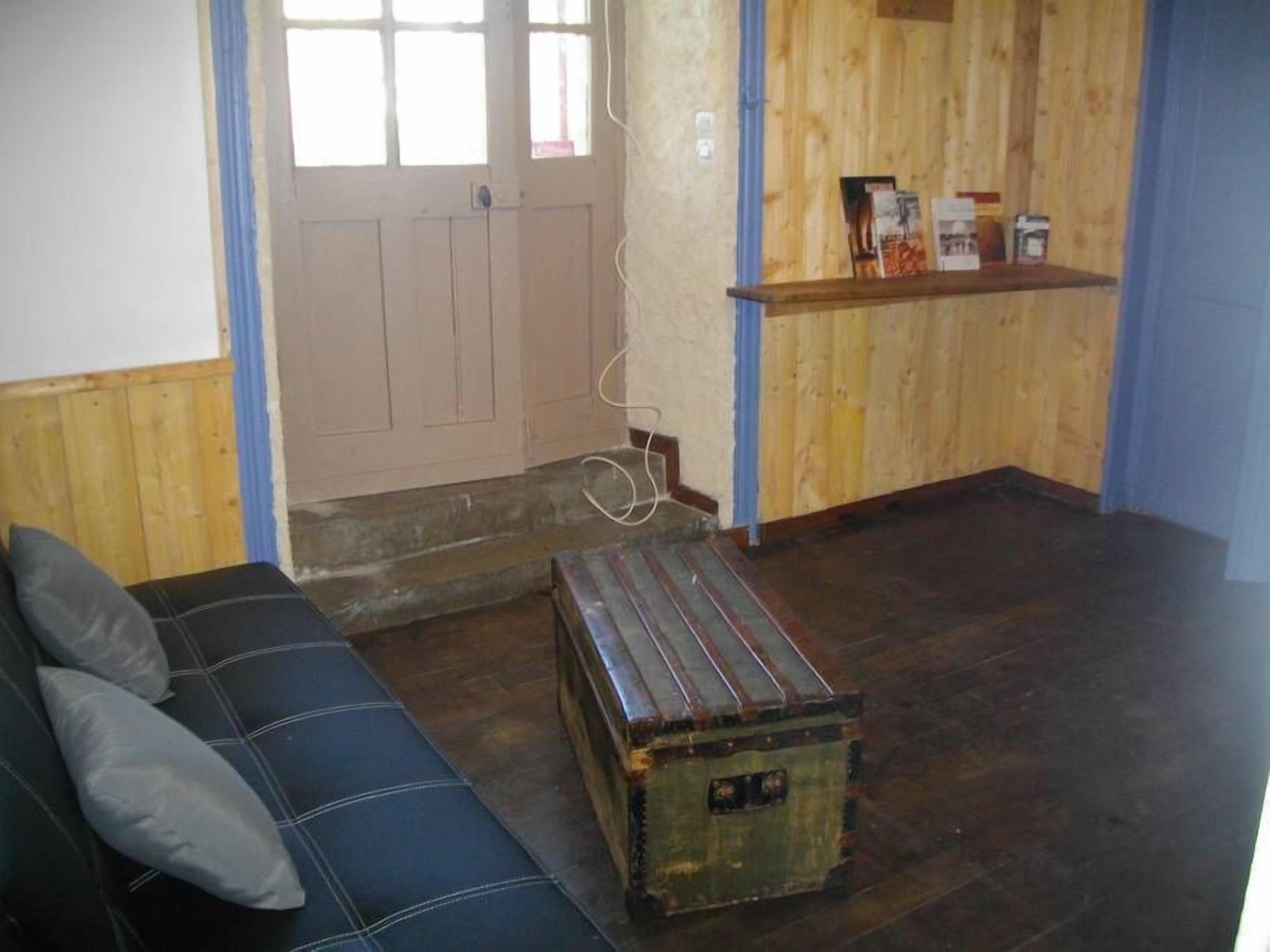 A room with a wooden floor, a blue sofa with cushions, a wooden cabinet with items on top, and a door with a window.