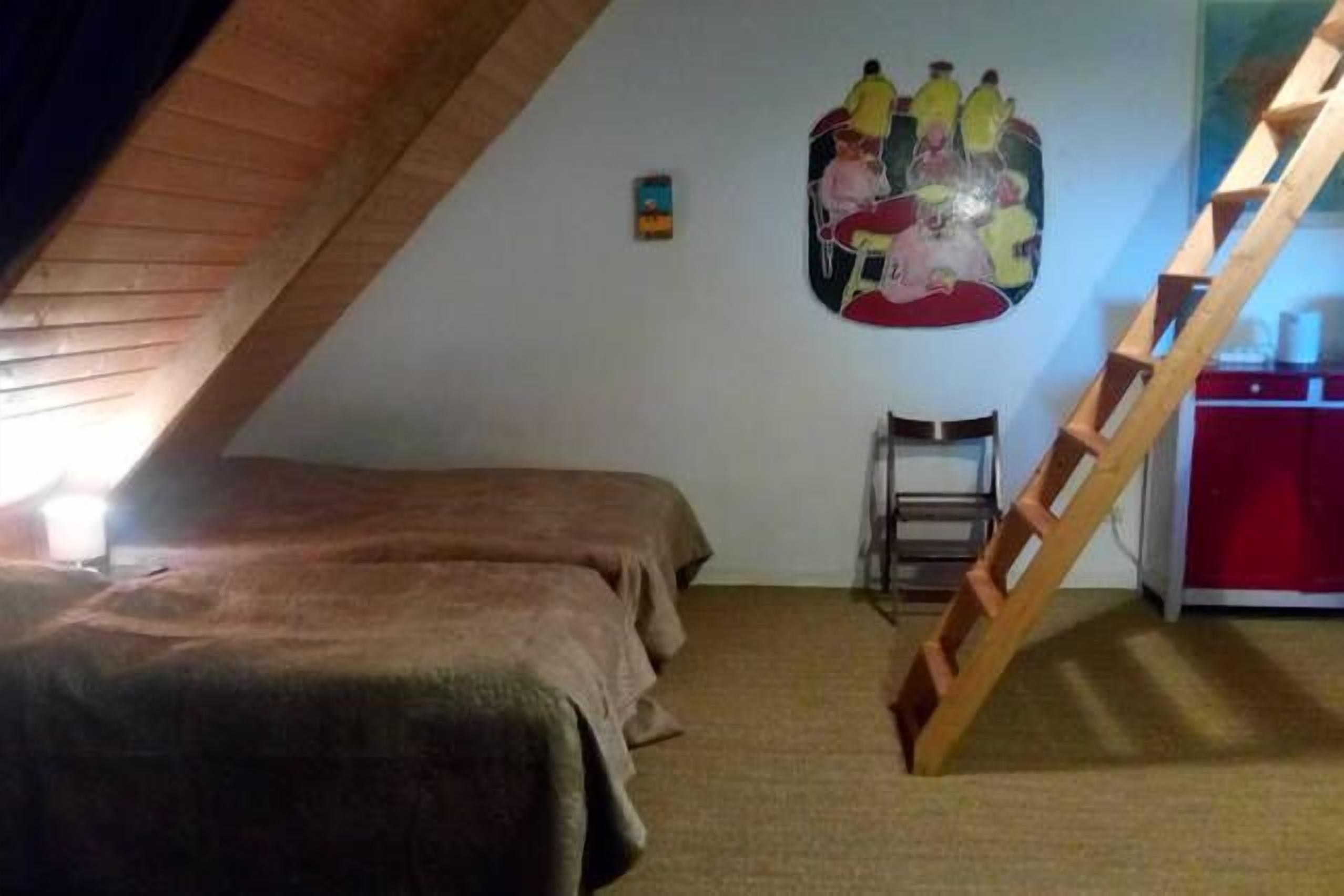 A bedroom with a sloped ceiling, a bed, a wooden ladder, and a wall-mounted artwork.