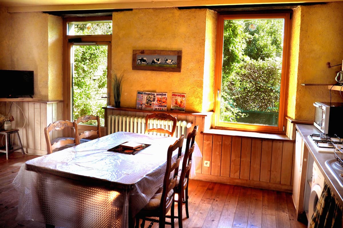 Una cocina acogedora con armarios de madera, una mesa de comedor con sillas, un radiador y una ventana con vistas al verdor.