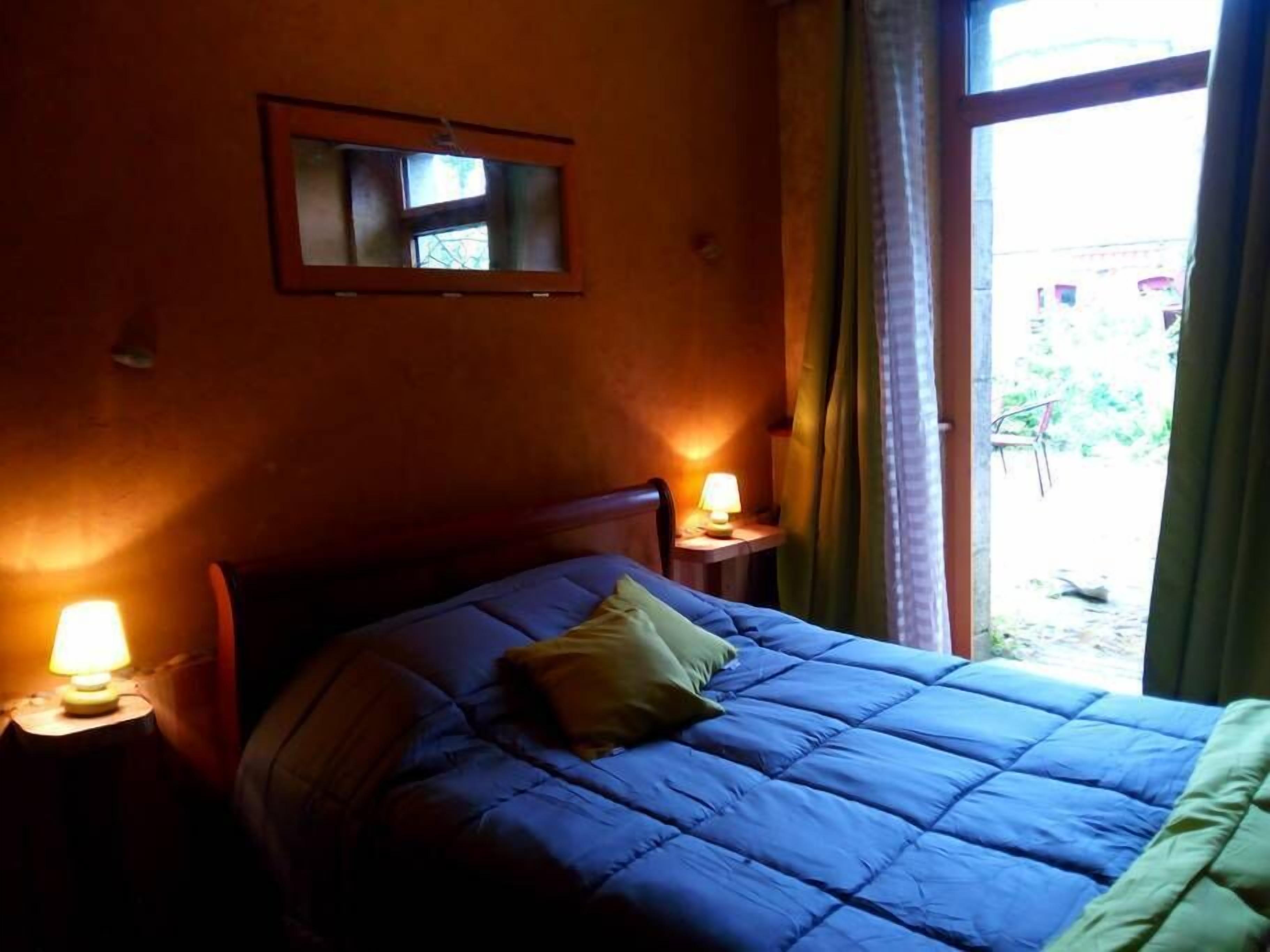 Een slaapkamer met een bed, twee bedlampen, een raam en een spiegel aan de muur.