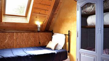 Una cama individual con cabecera, una ventana y un armario en una habitación con paredes de madera y techo inclinado.