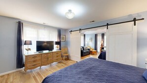 Ein Schlafzimmer mit Bett, Kommode, Fernseher und einer Schiebetür zu einem anderen Raum.