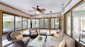 Ein Wintergarten mit Korbmöbeln, großen Fenstern und Deckenventilatoren.