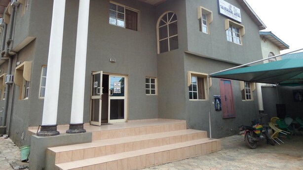 A two-story building with a central entrance, steps leading up to the entrance, and a covered area with chairs.