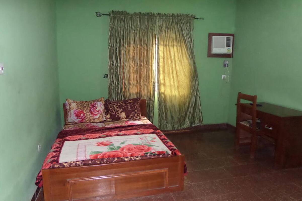 A bedroom with a bed, a chair, a curtain, and a wall-mounted air conditioner.