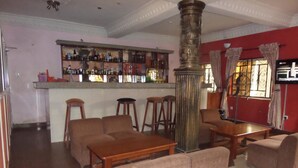 A bar area with stools, a bar counter with various bottles, and a television. There are sofas and a wooden table in the seating area.