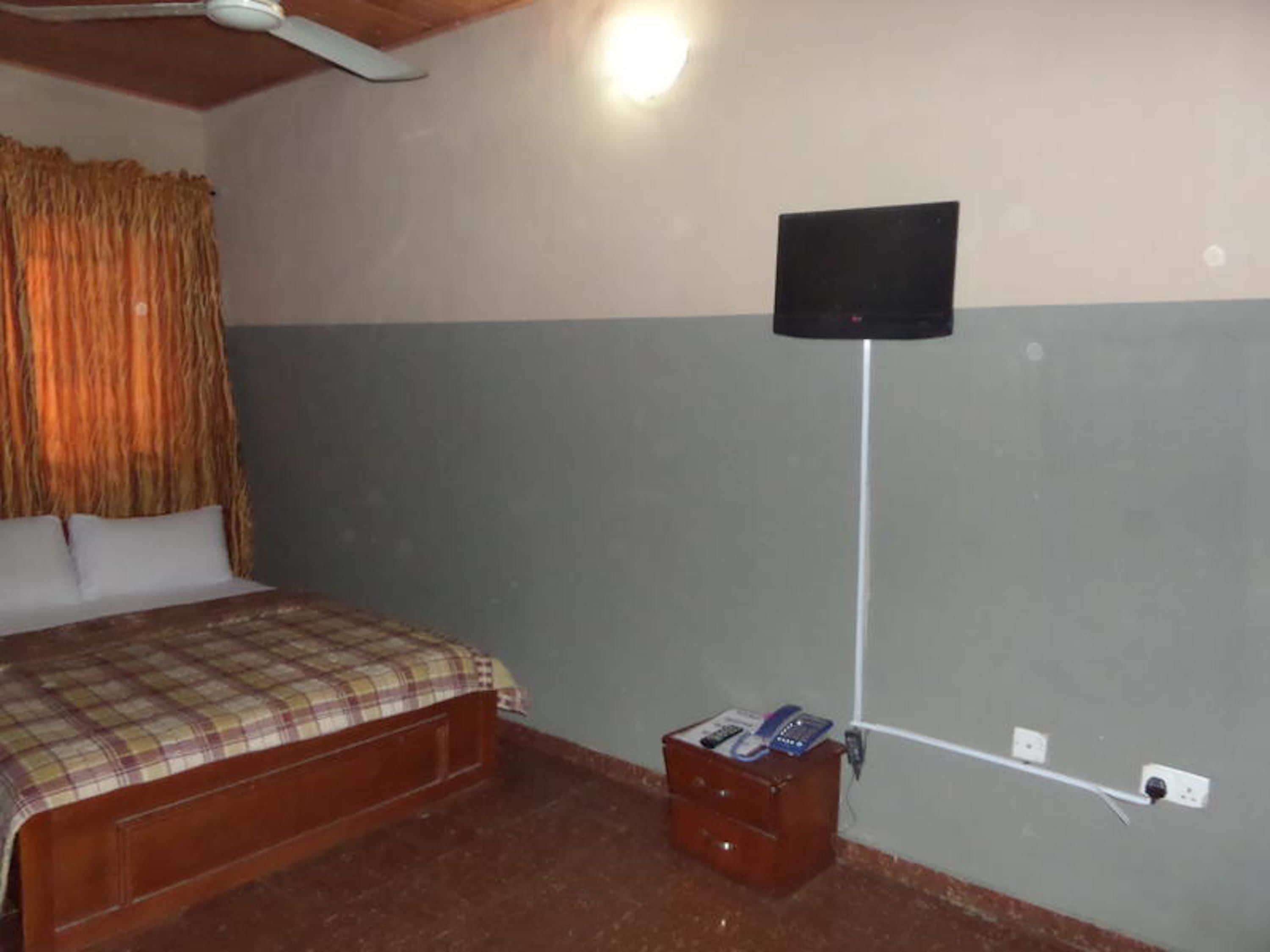 A bedroom with a bed, a television mounted on the wall, and a small wooden cabinet.
