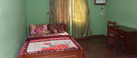 A bedroom with a wooden bed, green walls, a window with curtains, a desk, and an air conditioning unit.