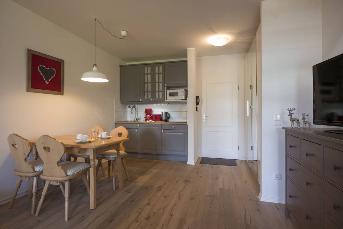 Een compacte keuken met houten kastjes, een eettafel met stoelen, een magnetron en een televisie.
